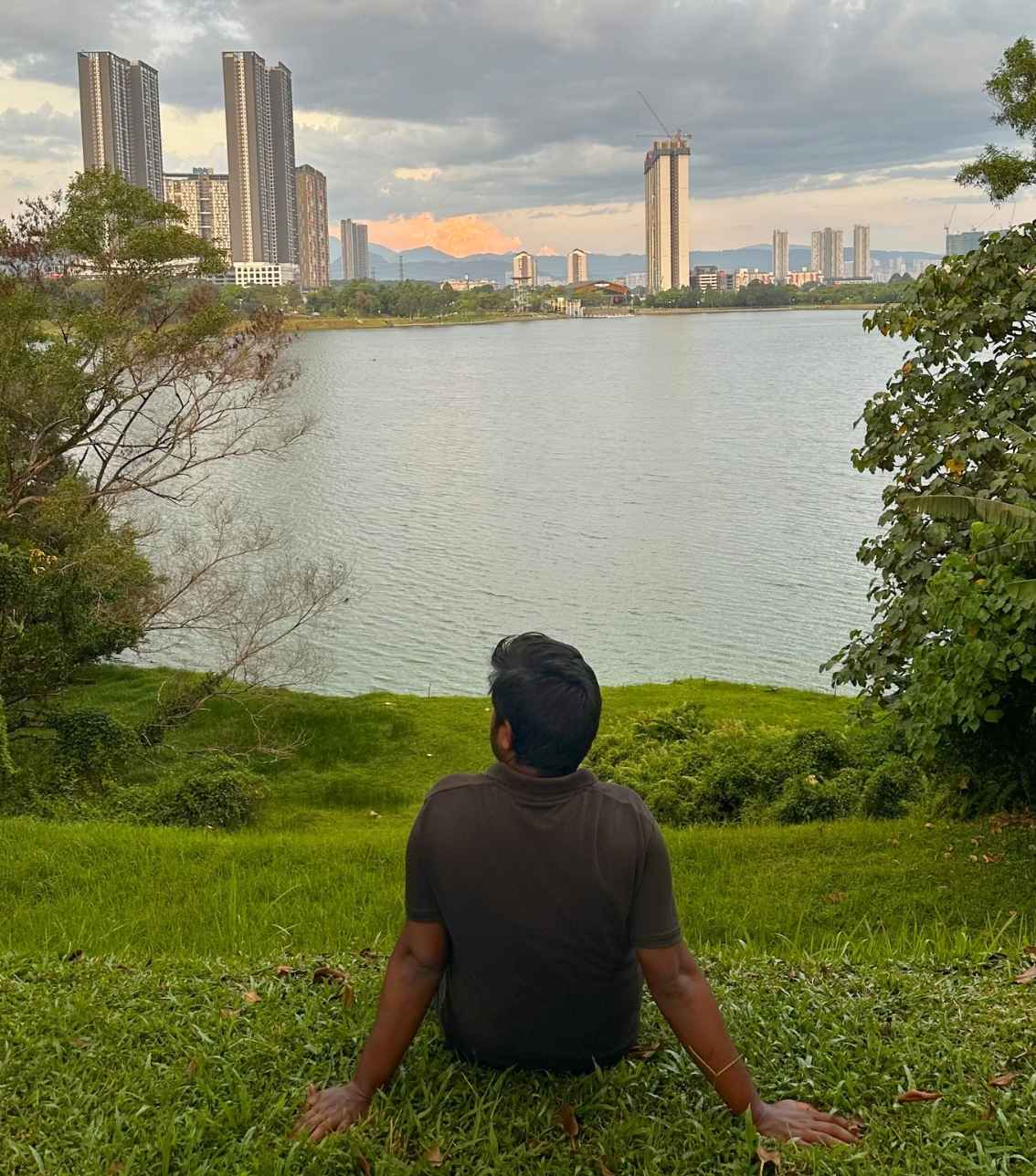 Mo sitting on green grass by a lake, reflecting outdoors